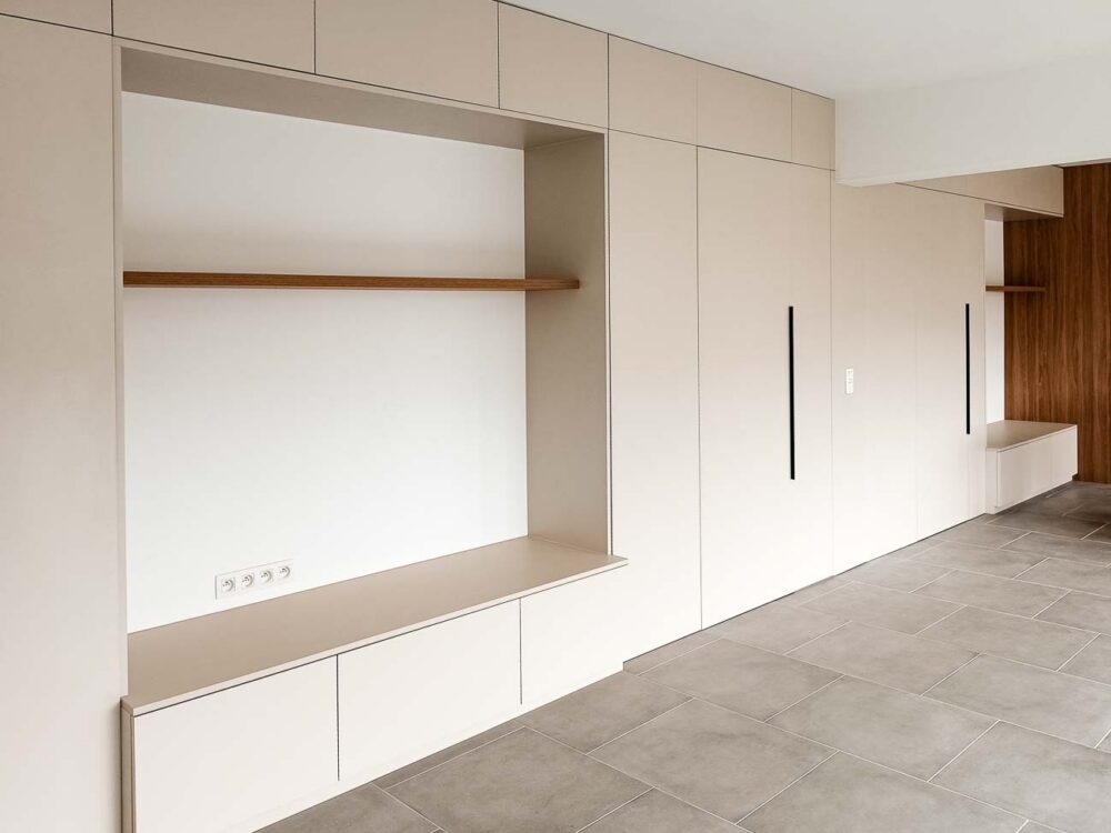Meubles de living beiges entièrement adaptés à la pièce, avec vestiaire et portes invisibles donnant accès à d’autres pièces
