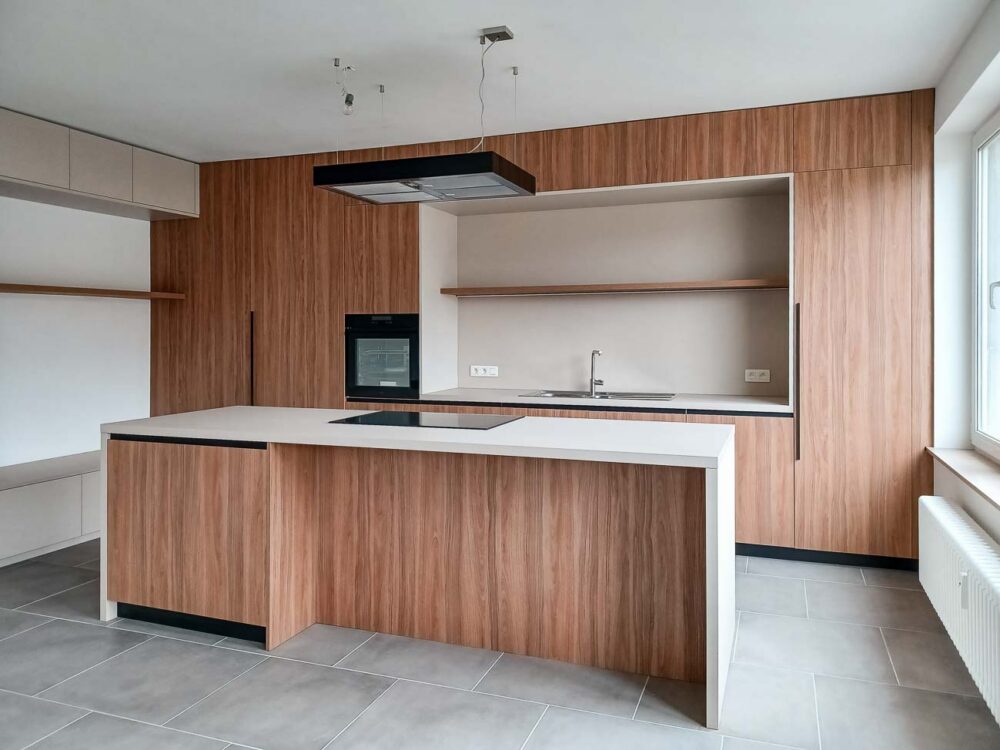 Cuisine en bois et gris beige avec long mur entièrement meublé de rangements sur mesure avec portes invisibles donnant accès aux autres pièces