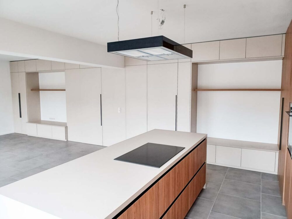 Cuisine en bois et gris beige avec long mur entièrement meublé de rangements sur mesure avec portes invisibles donnant accès aux autres pièces