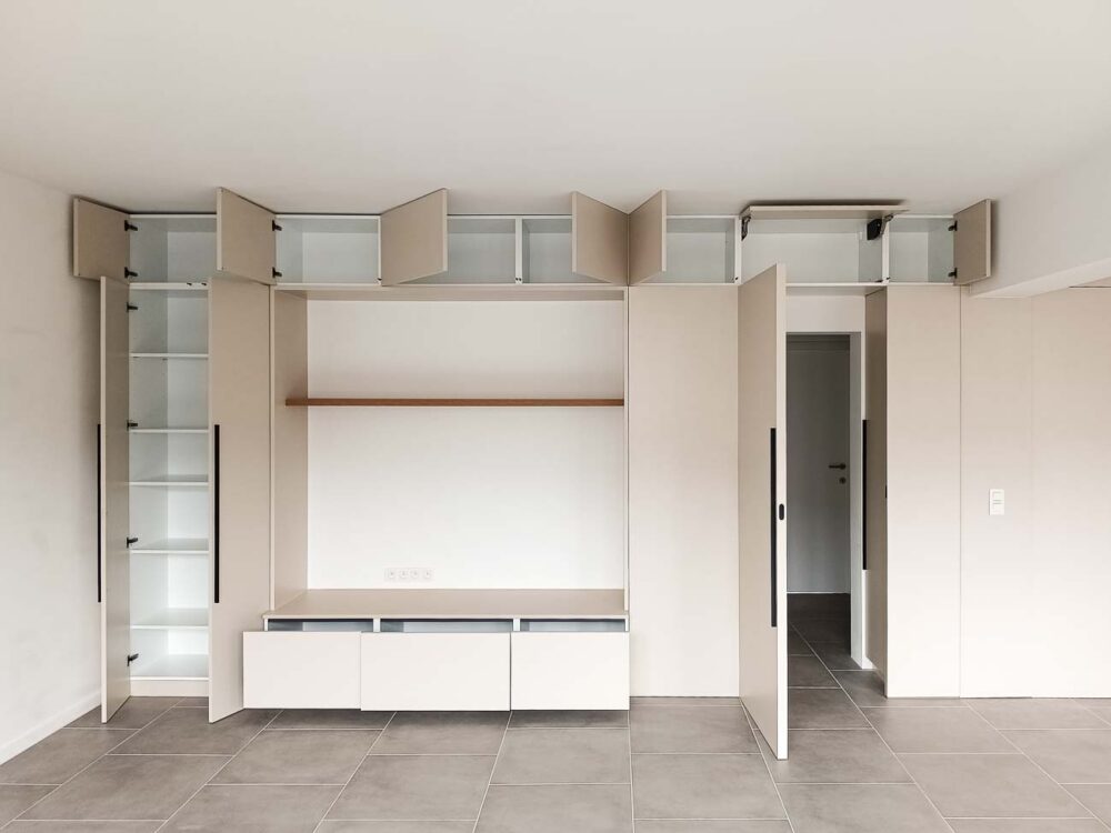Meubles de living beiges entièrement adaptés à la pièce, avec vestiaire et portes invisibles donnant accès à d’autres pièces