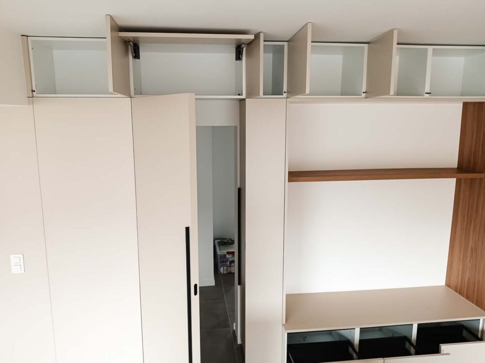 Meubles de living beiges entièrement adaptés à la pièce, avec vestiaire et portes invisibles donnant accès à d’autres pièces