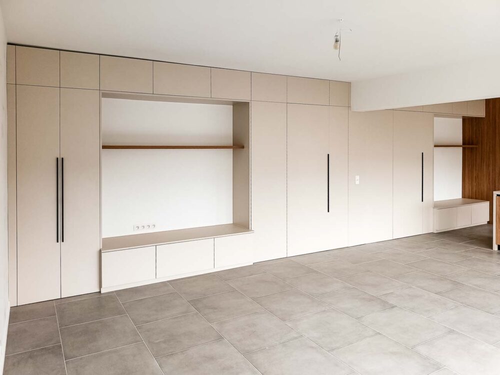 Meubles de living beiges entièrement adaptés à la pièce, avec vestiaire et portes invisibles donnant accès à d’autres pièces