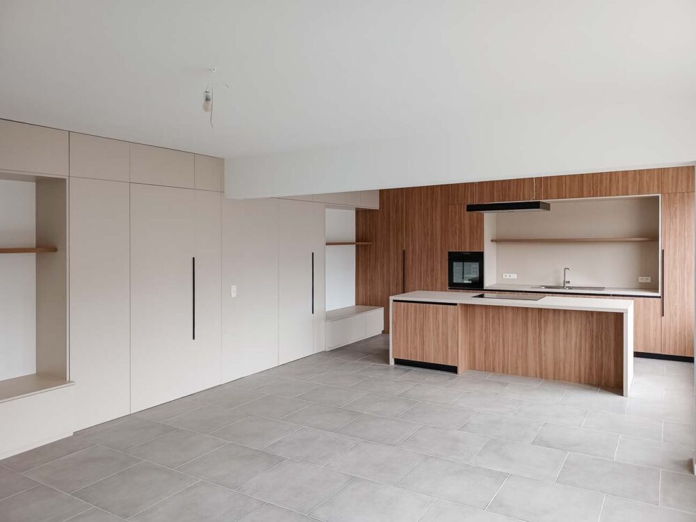 Cuisine en bois et gris beige avec long mur entièrement meublé de rangements sur mesure avec portes invisibles donnant accès aux autres pièces