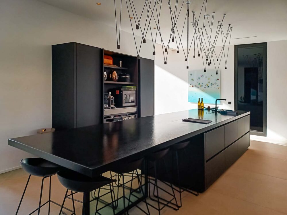 Cuisine intégralement noire, en verre mat et plan de travail en pierre naturelle. Colonnes à portes rentrantes