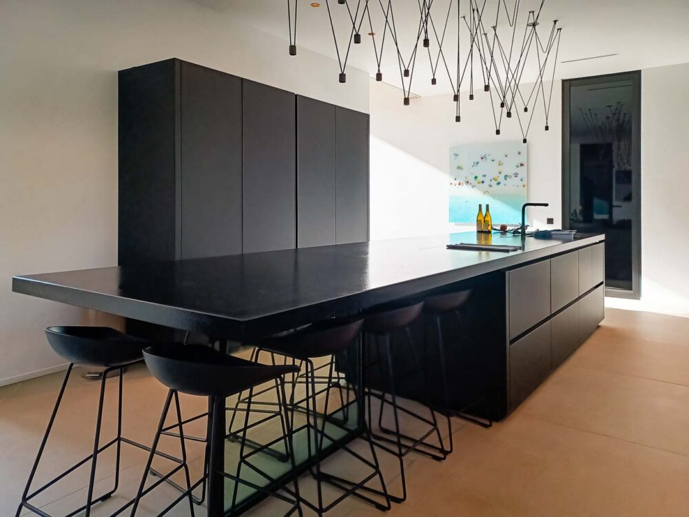 Cuisine intégralement noire, en verre mat et plan de travail en pierre naturelle. Colonnes à portes rentrantes