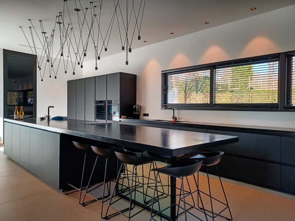 Cuisine intégralement noire, en verre mat et plan de travail en pierre naturelle. Colonnes à portes rentrantes