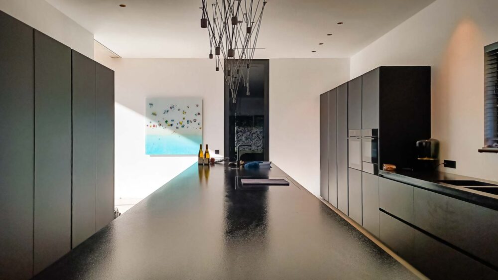 Cuisine intégralement noire, en verre mat et plan de travail en pierre naturelle. Colonnes à portes rentrantes