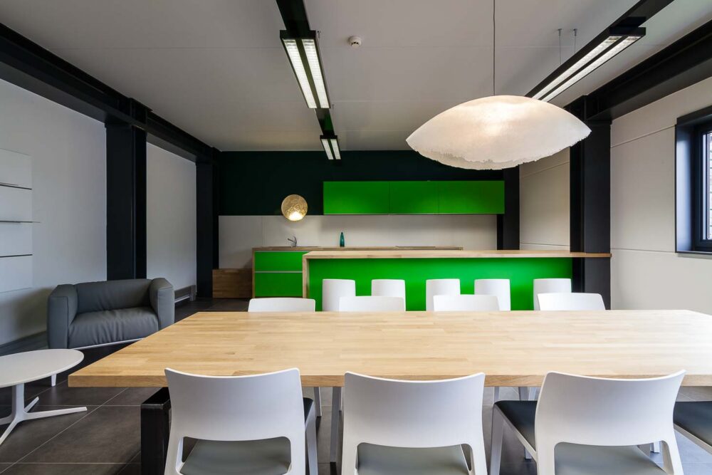 Cuisine d’entreprise en verre vert et bois massif, avec luminaires et salle de réunion