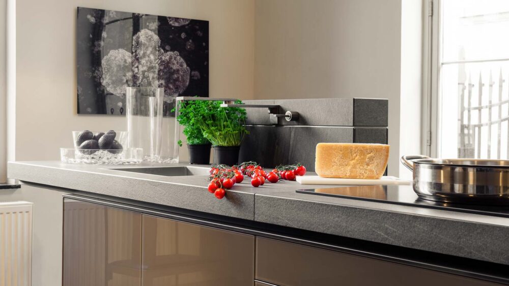 Cuisine avec plan de travail massif en pierre et grandes colonnes en verres gris brillant suspendues, évier en pierre haut de gamme