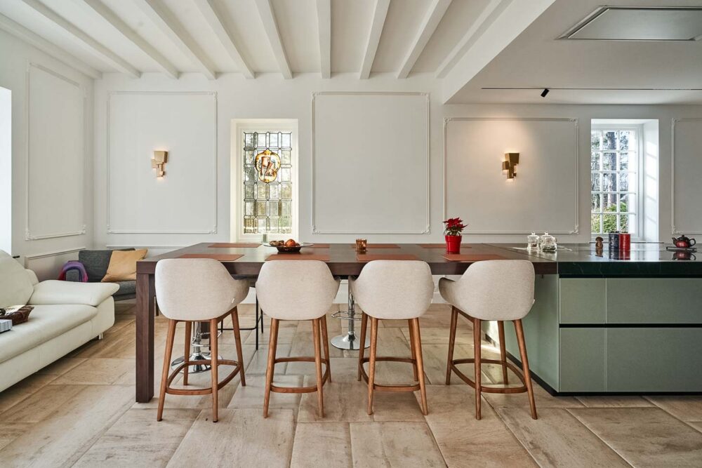 Cuisine spacieuse haut de gamme avec plan de travail en pierre naturelle vert foncé quartzite, îlot central en verre vert olive, détails en cuivre (Inox PVD) et composition murale en noyer foncé