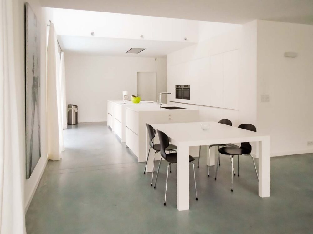 Cuisine design minimaliste avec trois îlots cubiques en verre avec plan de travail en Corian blanc, composition murale en laqué mat et hotte plafond sur mesure