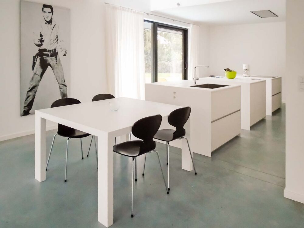 Cuisine design minimaliste avec trois îlots cubiques en verre avec plan de travail en Corian blanc, composition murale en laqué mat et hotte plafond sur mesure