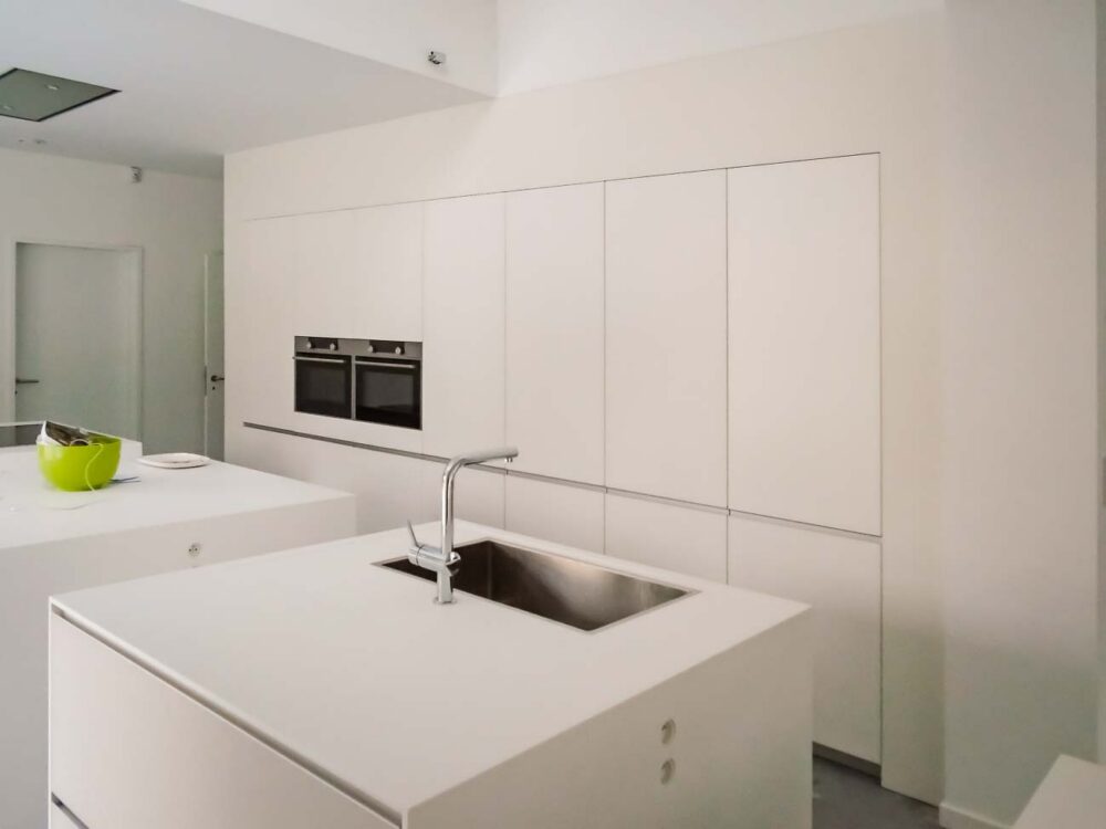 Cuisine design minimaliste avec trois îlots cubiques en verre avec plan de travail en Corian blanc, composition murale en laqué mat et hotte plafond sur mesure
