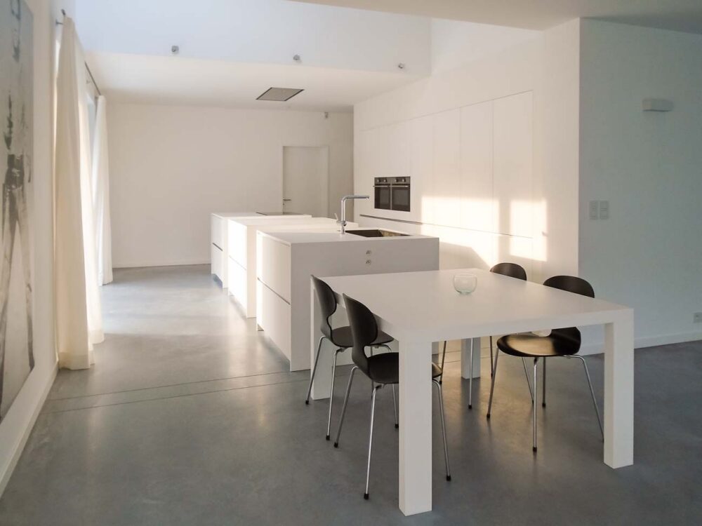 Cuisine design minimaliste avec trois îlots cubiques en verre avec plan de travail en Corian blanc, composition murale en laqué mat et hotte plafond sur mesure