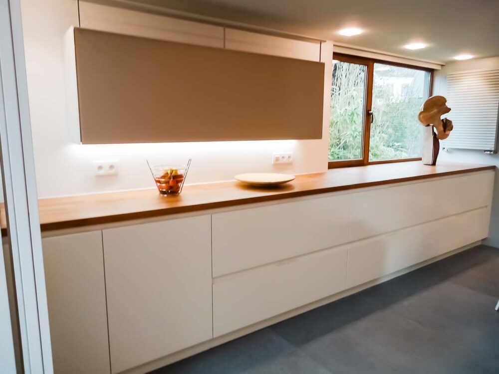 Cuisine blanche, verre blanc mat, plan de travail en bois massif et colonnes en laqués gris mat avec porte dissimulée, accès buanderie