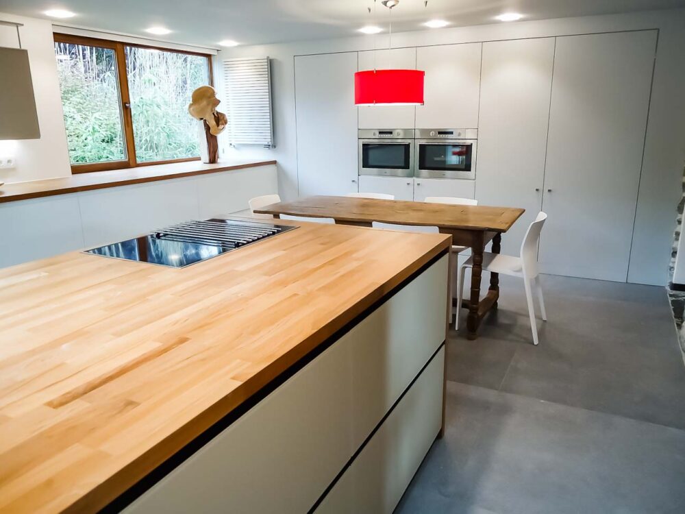 Cuisine blanche, verre blanc mat, plan de travail en bois massif et colonnes en laqués gris mat avec porte dissimulée, accès buanderie