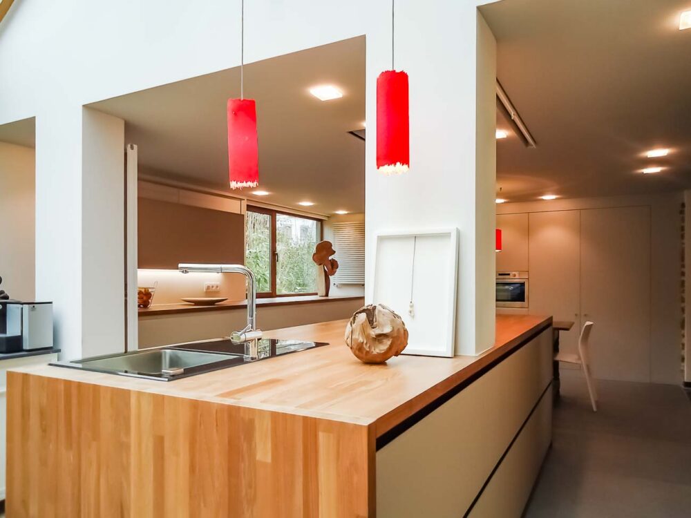 Cuisine blanche, verre blanc mat, plan de travail en bois massif et colonnes en laqués gris mat avec porte dissimulée, accès buanderie