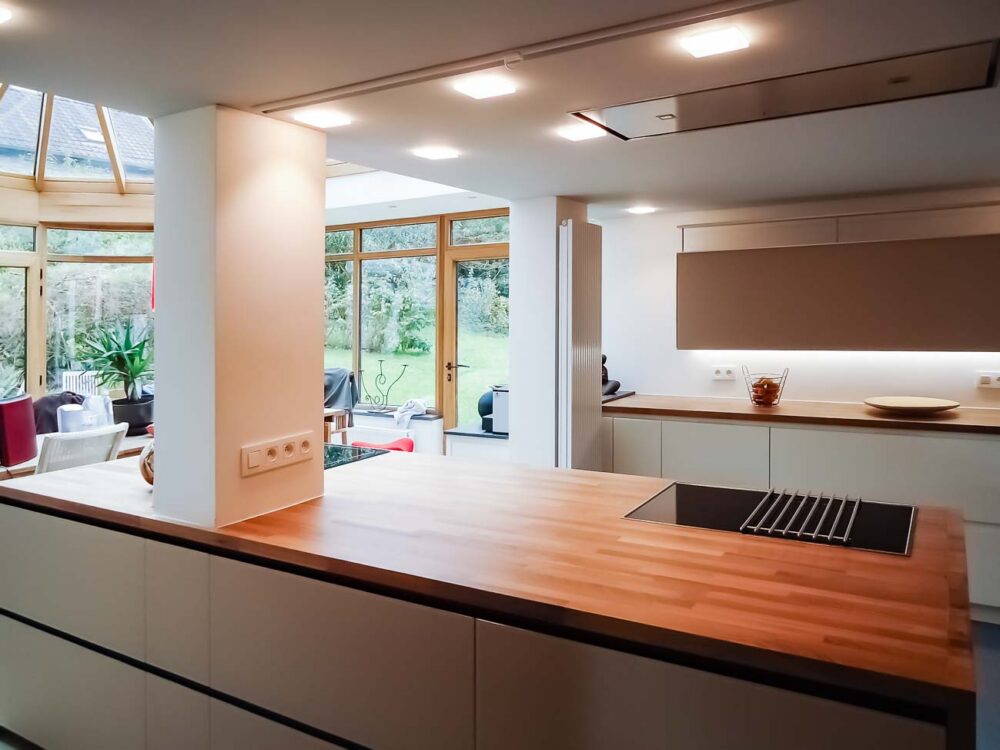 Cuisine blanche, verre blanc mat, plan de travail en bois massif et colonnes en laqués gris mat avec porte dissimulée, accès buanderie