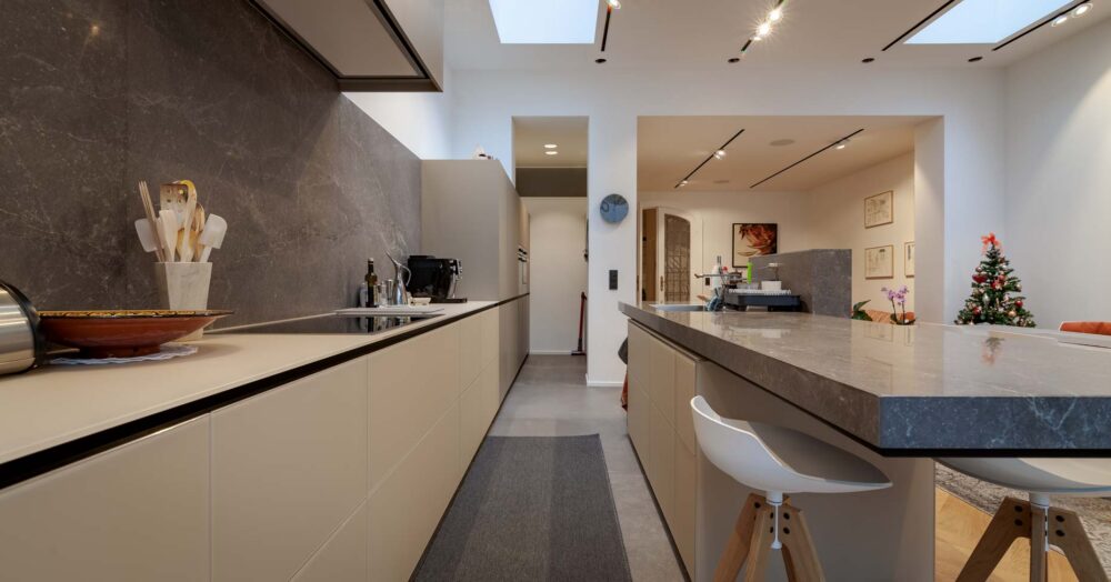 Cuisine avec meubles bas en verre gris et colonnes en stratifié gris. Plan de travail en pierre naturelle