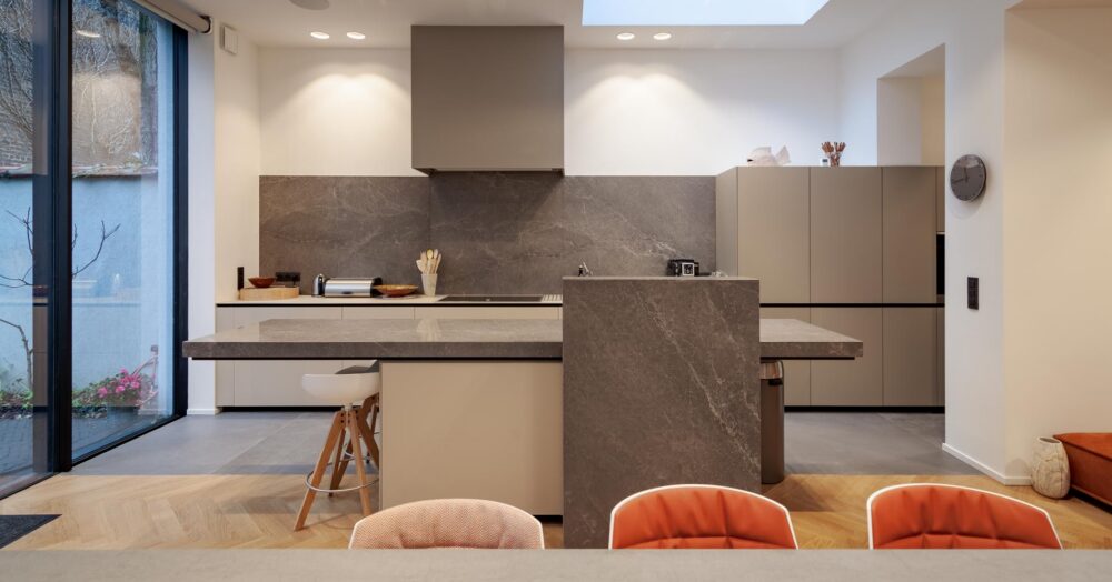 Cuisine avec meubles bas en verre gris et colonnes en stratifié gris. Plan de travail en pierre naturelle