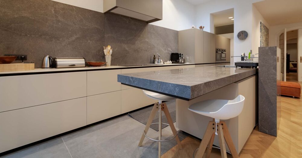 Cuisine haut de gamme avec meubles bas en verre gris et colonnes en stratifié gris. Plan de travail en pierre naturelle flottant en porte-à-faux