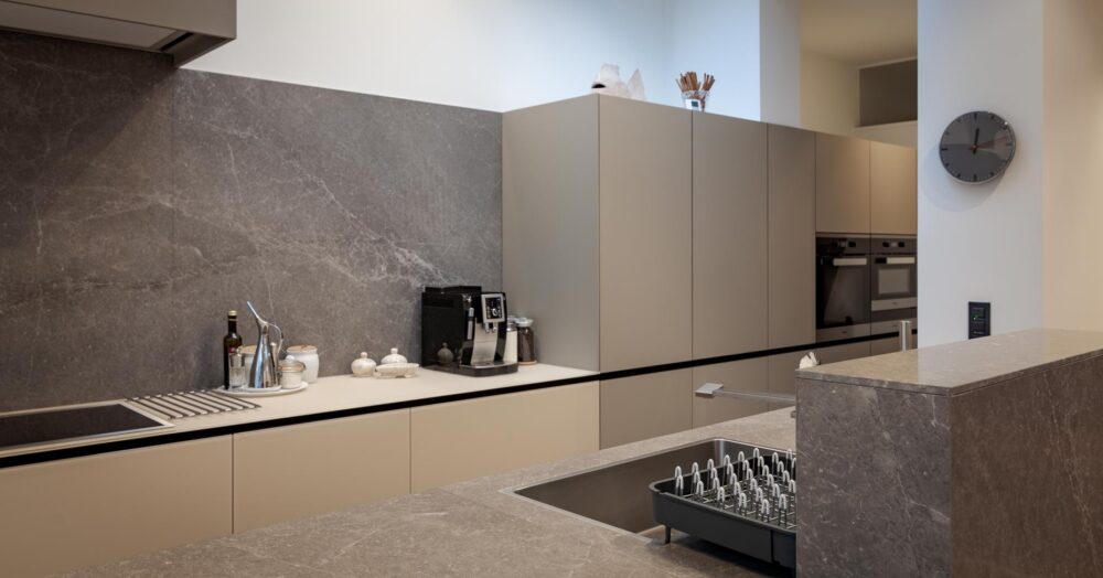 Cuisine avec meubles bas en verre gris et colonnes en stratifié gris. Plan de travail en pierre naturelle