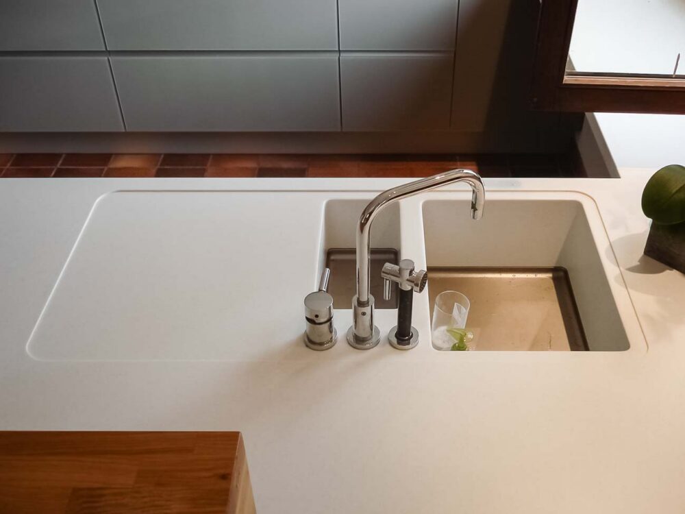 Cuisine en verre gris et plan de travail en Corian blanc avec coin snack en bois massif