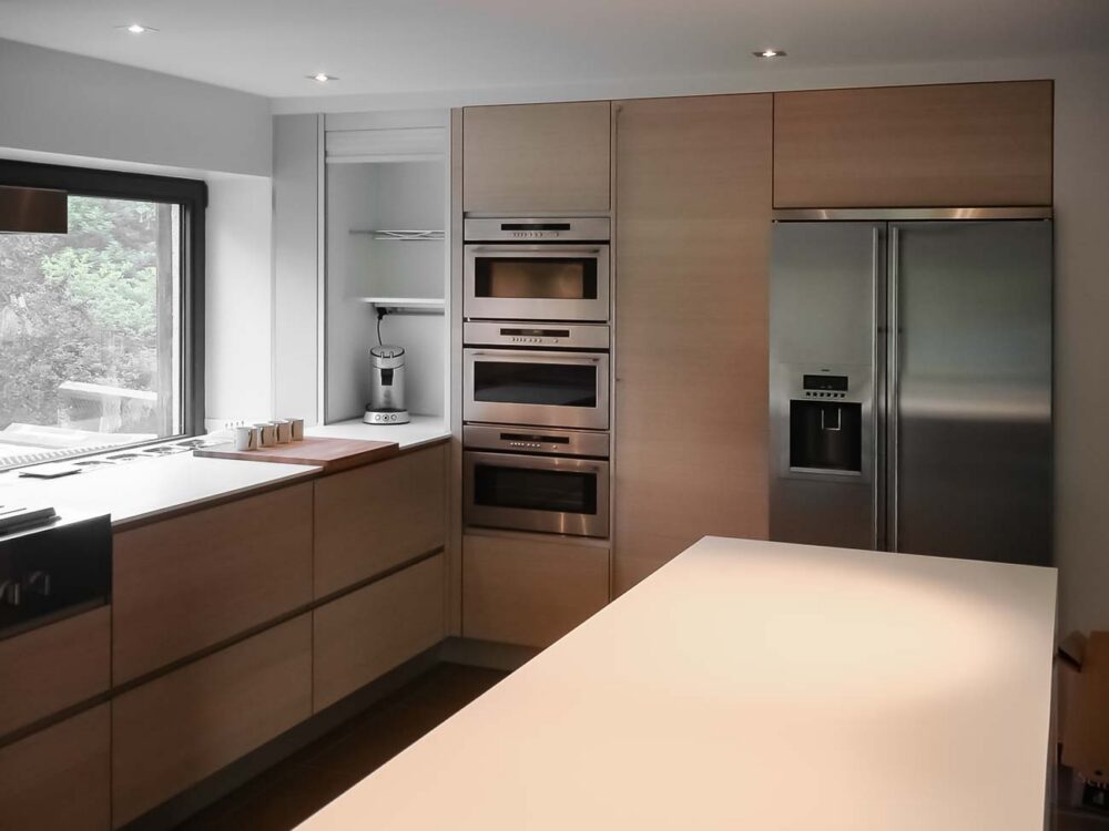 Cuisine entièrement équipée avec îlot monolithe en Corian blanc et portes en plaqué chêne et aluminium