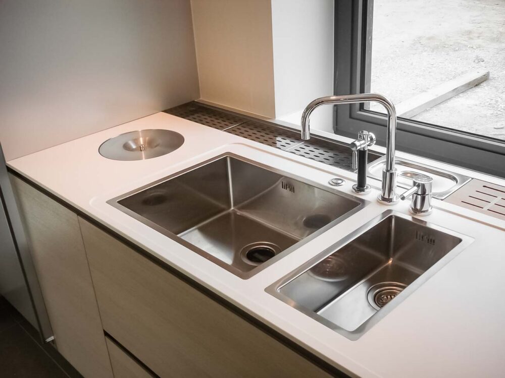 Cuisine entièrement équipée avec îlot monolithe en Corian blanc et portes en plaqué chêne et aluminium - détail évier sur mesure