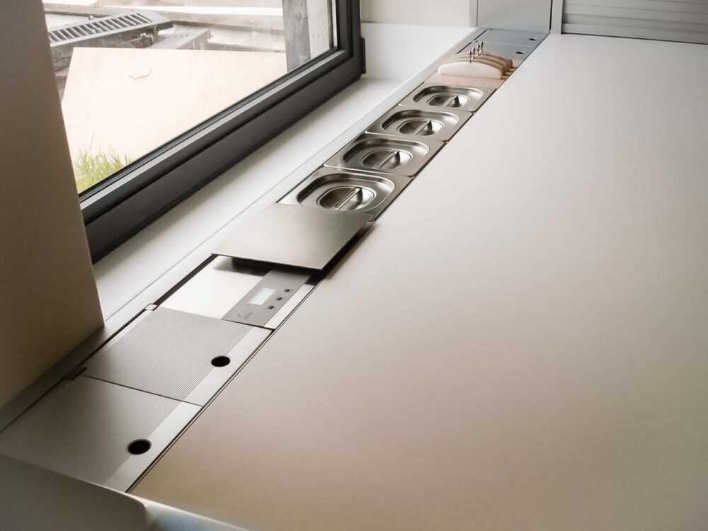Cuisine entièrement équipée avec îlot monolithe en Corian blanc et portes en plaqué chêne et aluminium - détail haut de gamme