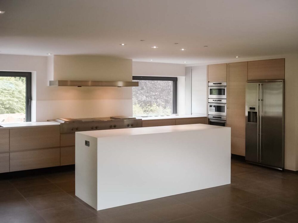 Cuisine entièrement équipée avec îlot monolithe en Corian blanc et portes en plaqué chêne et aluminium