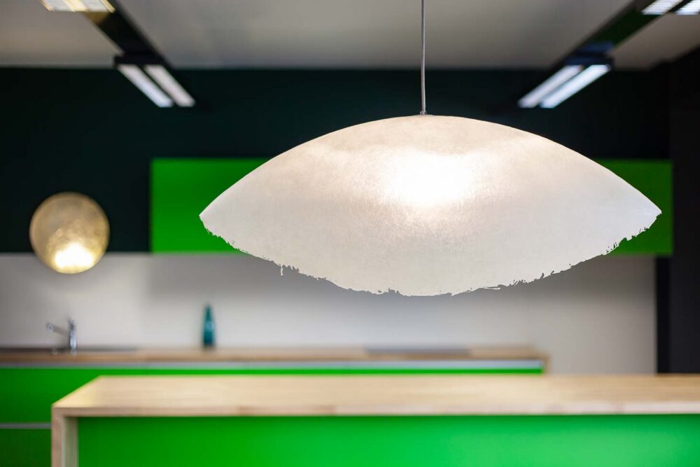 Cuisine d’entreprise en verre vert et bois massif, avec luminaires et salle de réunion